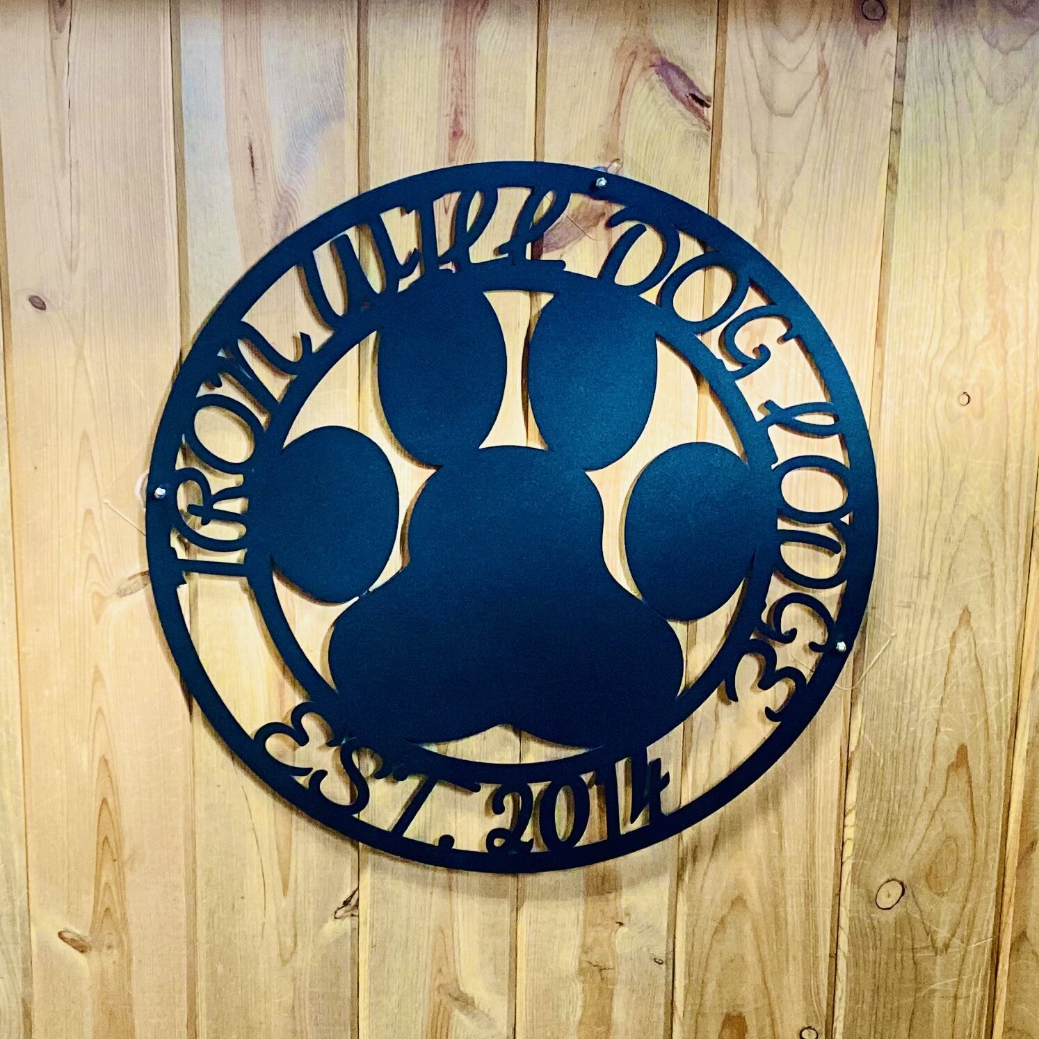 A black metal sign with the name of a dog and its paw.